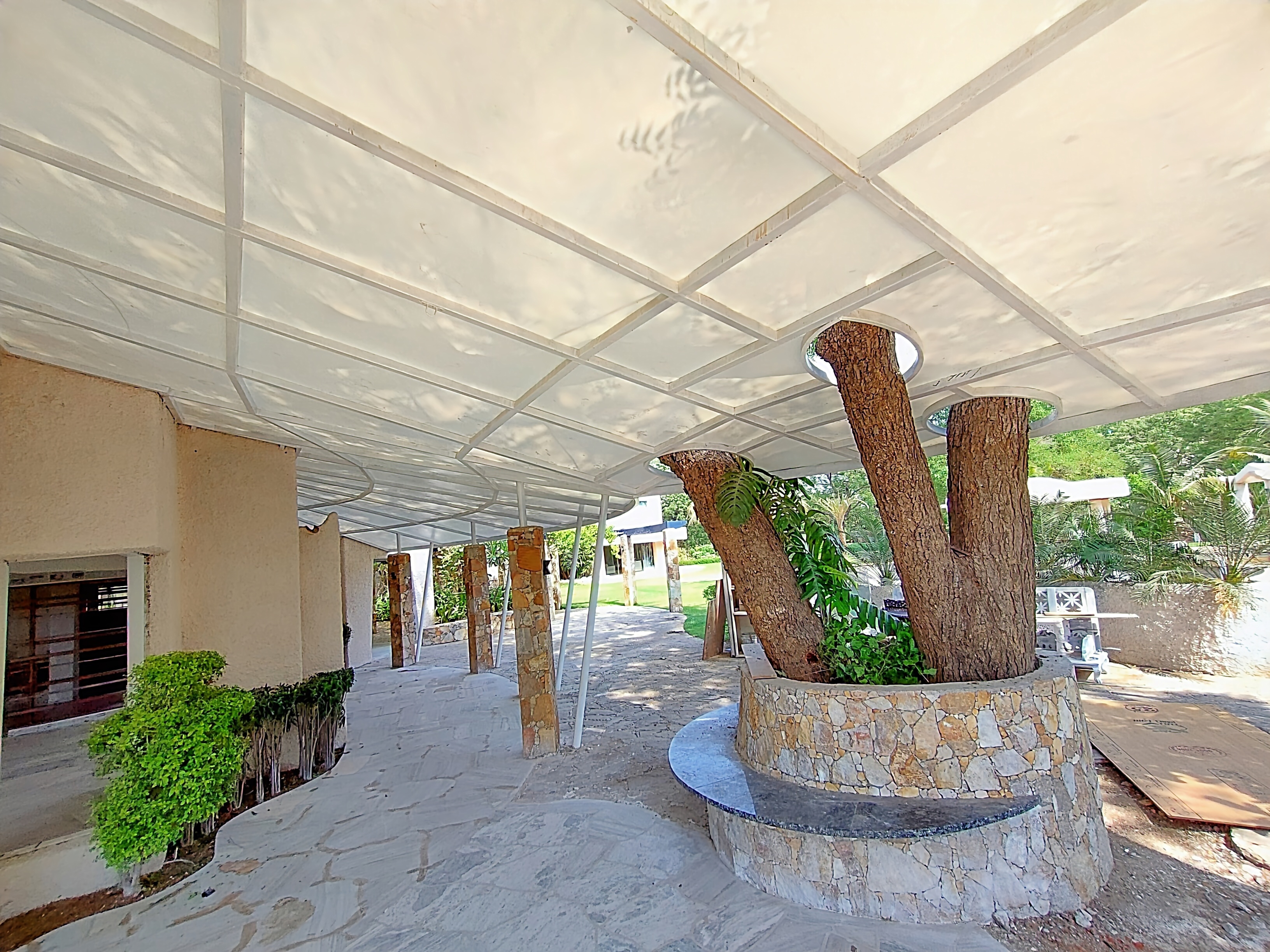 Flat tensile canopy over a stone-paved walkway with tree cutouts