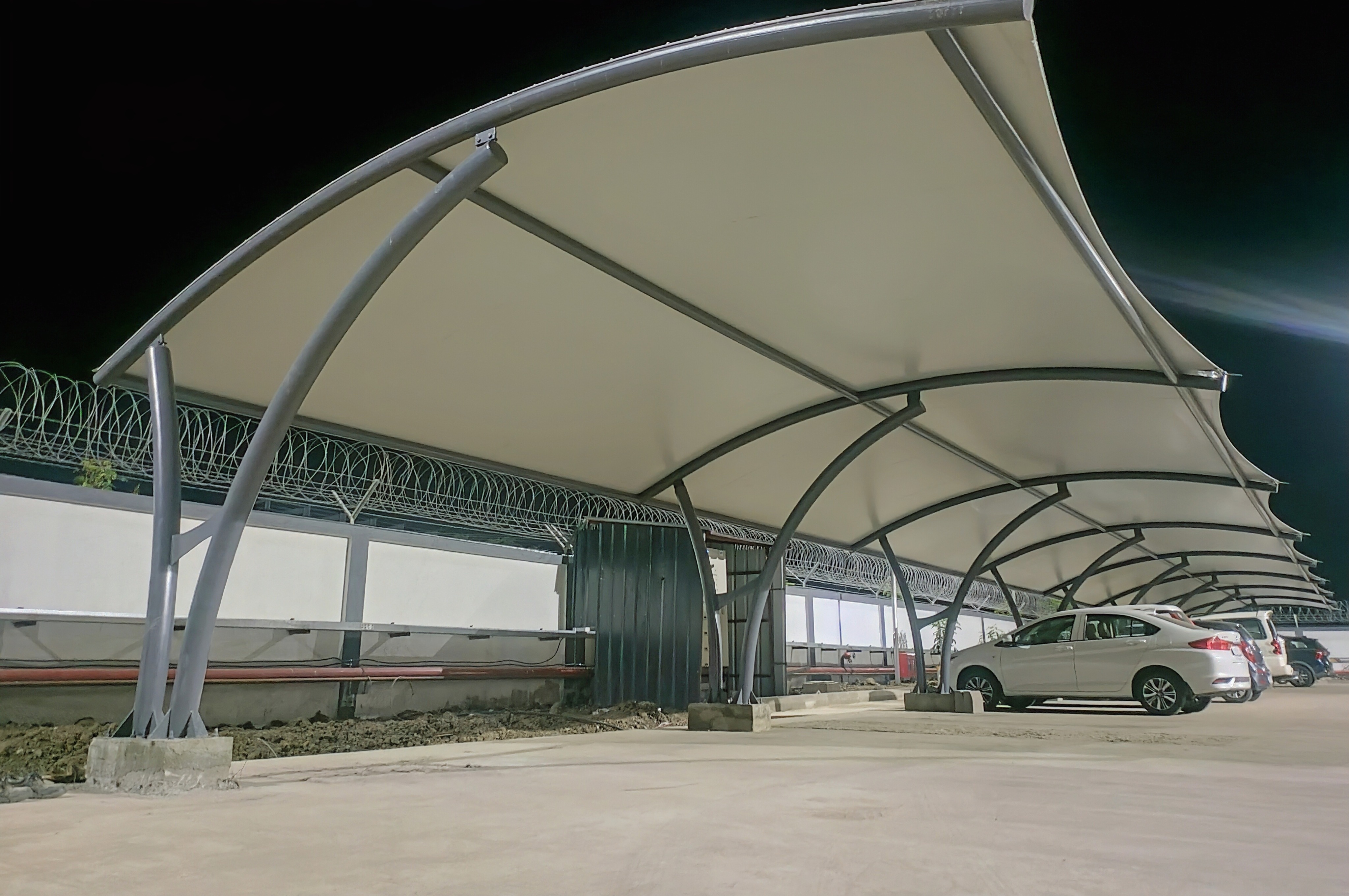 Sweeping cantilever fabric canopy installation at night, illuminated against a dark sky